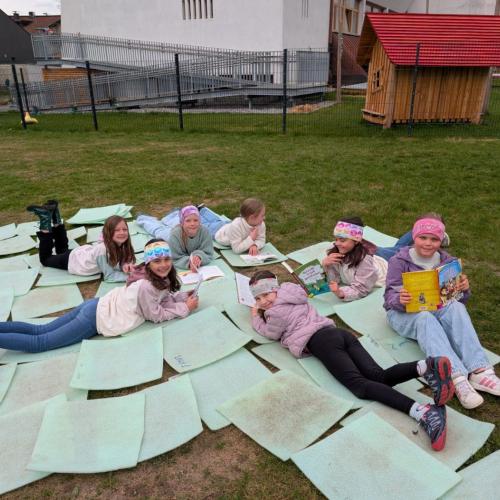 Gruppe von Kindern liegt auf Matten im Gras beim Lesen