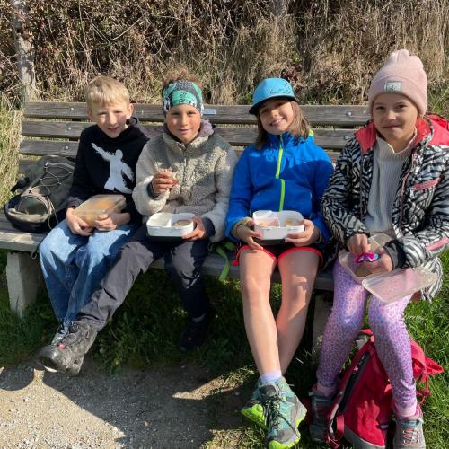 Kinder sitzen mit Jause auf Bank