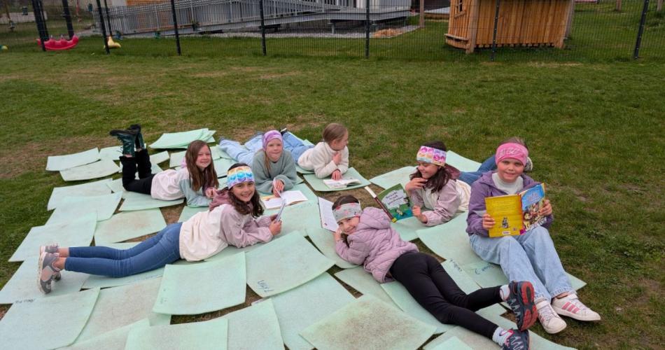 Gruppe von Kindern liegt auf Matten im Gras beim Lesen